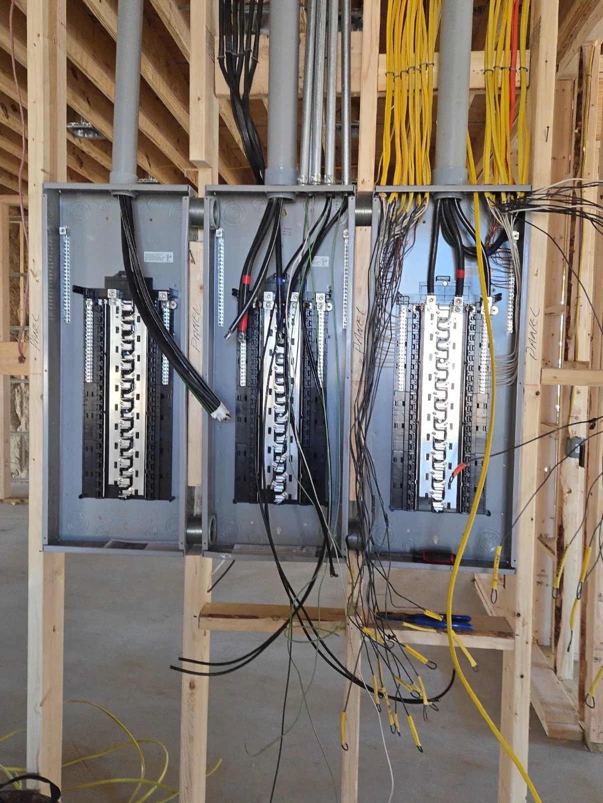 Three open electrical panels with wiring in a framed wall.
