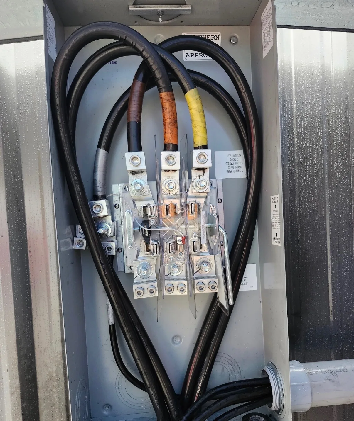 Heavy electrical service conductors connected to terminals.
